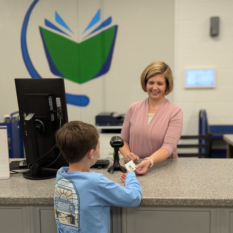 Woman behind library desk handing young boy a new library card