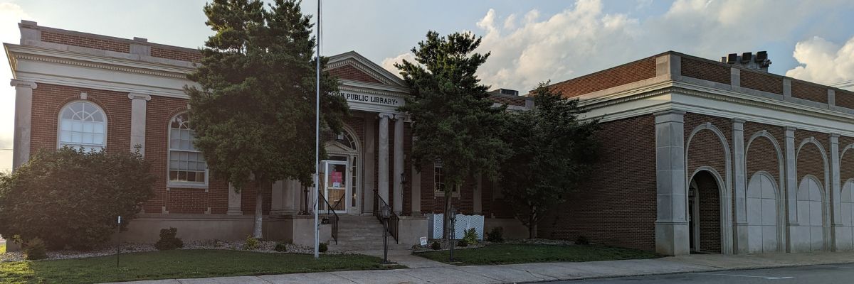 Front entrance of George Coon Public Library building, red brick with white neoclassical elements like columns and arches