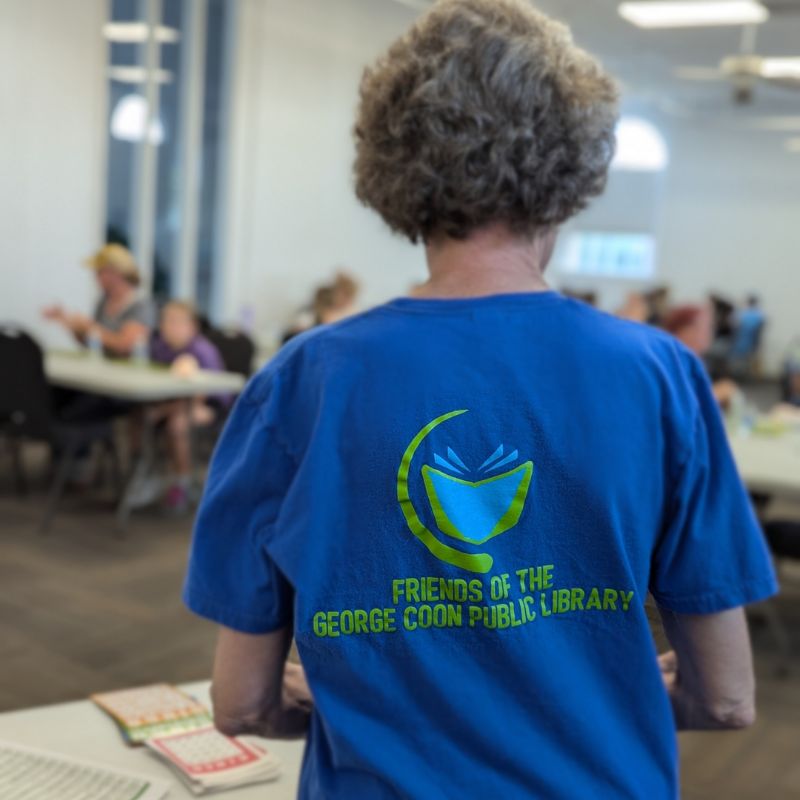 Friends volunteer wearing blue Friends of the George Coon Public Library t-shirt at bingo event