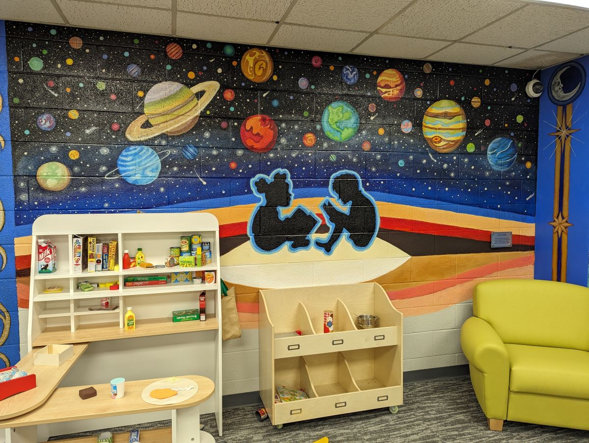 Colorful mural depicting two child silhouettes reading against a backdrop of planets and stars