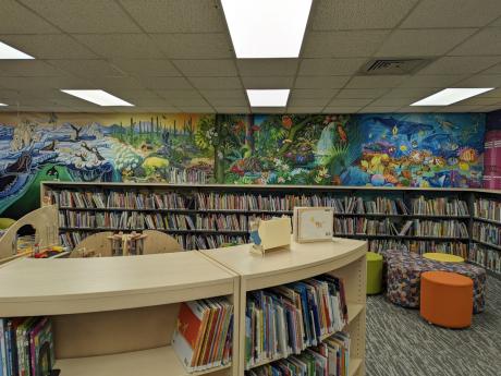 Photo of colorful murals over low shelves in the children's library; murals depict animals in ocean, forest, desert, and arctic environments