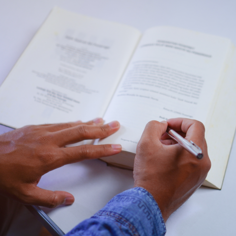 image of an open book as a person is holding an ink pen over the page as if to sign or write in the book.