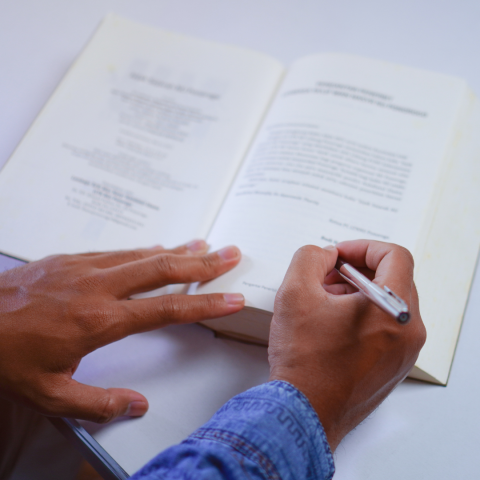 image of an open book as a person is holding an ink pen over the page as if to sign or write in the book.