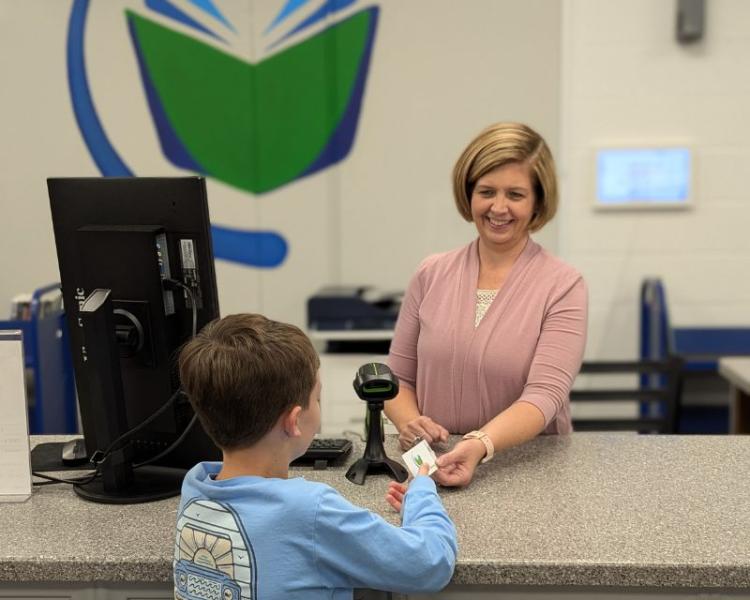 Woman behind library desk handing young boy a new library card